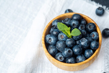 Fresh blueberries in a wooden bowl with a mint sprig on a light background