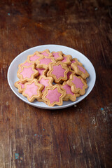 Star shaped cookies with pink frosting on white plate, wooden rustic background. Strawberry icing on cookies in shape of stars. Top view, copy space