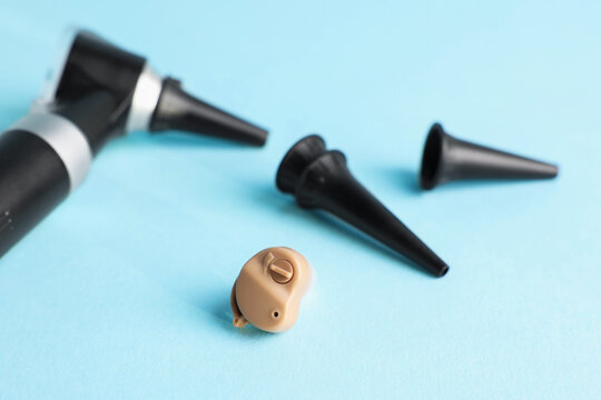 Modern otoscope, hearing aid and ear speculums on light blue background, closeup