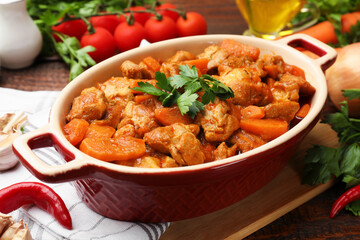 Delicious cooked stew in baking dish and fresh ingredients on wooden table, closeup