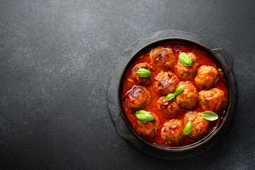 Meatballs in tomato sauce in iron plate on black background.