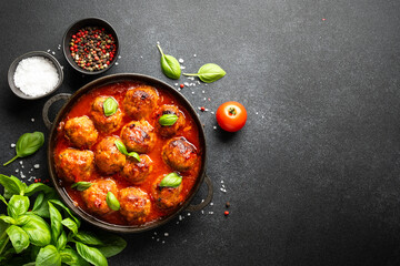 Meatballs in tomato sauce in iron plate on black background.