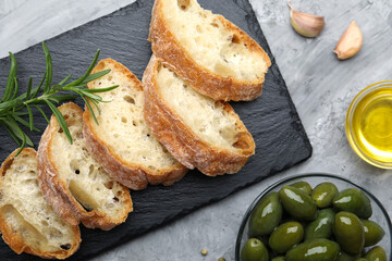 Slices of ciabatta, spices and olives on grey table, flat lay