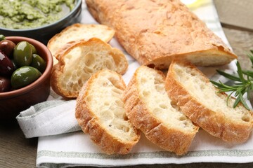 Cut ciabatta, spices and olives on wooden table, closeup