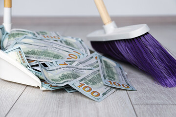 Sweeping dollar banknotes with broom into dustpan on light wooden floor, closeup