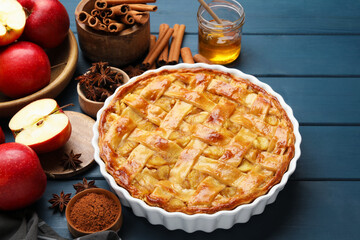 Delicious homemade apple pie in baking dish and ingredients on blue wooden table, closeup