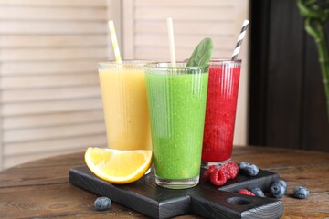 Different tasty smoothies in glasses and ingredients on wooden table, closeup