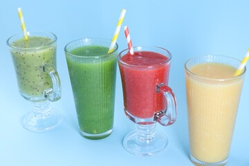 Different tasty smoothies in glasses on light blue background, closeup