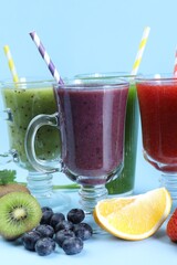 Different tasty smoothies in glasses and ingredients on light blue background, closeup