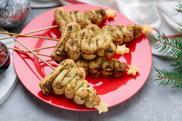 Christmas tree shaped snacks made with puff pastry, pesto sauce, cheese and festive decor on grey table, closeup