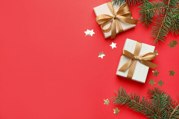 Fir tree branches, gifts and Christmas decor on red background, flat lay. Space for text