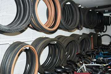 Multiple bicycle tires and inner tubes hanging on wall racks above row of parked bicycles in storage or workshop setting, showing organized arrangement of cycling equipment and spare parts