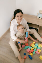 Young happy mother playing game with educational pyramid with cute little child girl in the living room at home. Woman parent spending time with daughter. Family leisure and people concept.