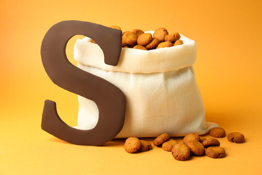 Sinterklaas (Saint Nicholas) Day. Chocolate letter S and kruidnoten cookies in sack on pale orange background