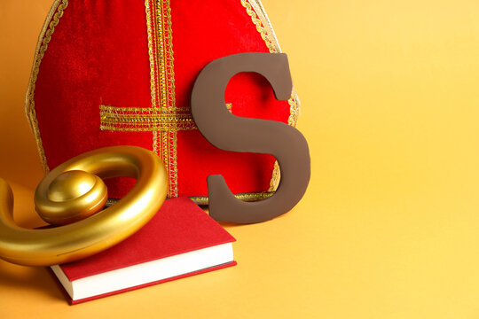 Sinterklaas (Saint Nicholas) Day. Chocolate letter S, mitre, crosier and notebook on pale orange background, closeup. Space for text - Powered by Adobe