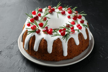 Tasty Christmas cake with icing, cranberries and rosemary on black table, closeup
