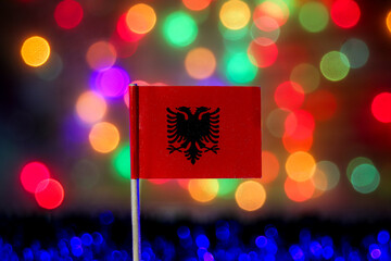 The Albania flag with the double-headed eagle is set against a vibrant, abstract rainbow bokeh. Perfect for Independence Day, Balkan travel, and European identity.