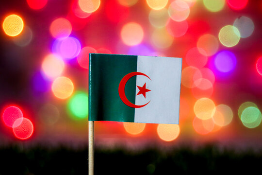The Algeria flag with its star and crescent shines against a vibrant, abstract rainbow bokeh. Perfect for Revolution Day, North Africa, Maghreb culture, or festive events. - Powered by Adobe