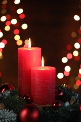 Burning candles, fir tree branches, cones and baubles against black background with blurred lights, closeup. Bokeh effect