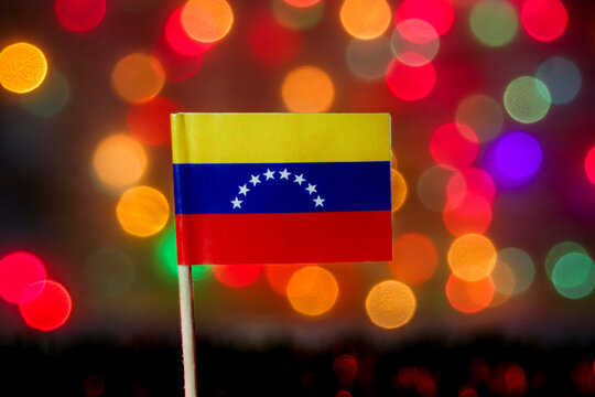 The Venezuelan flag (tricolor with arc of stars) set against a vibrant, festive bokeh background. Highly relevant for politics, economics, and Independence Day celebrations.