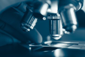 Macro photo of optical microscope lens focusing on sample slide under sterile laboratory lighting. Symbolizes technology, research, and medical discovery.
