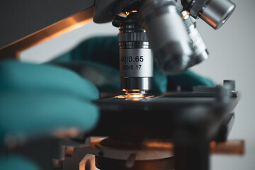 High-quality close-up image of a laboratory microscope being adjusted by a scientist in gloves. Represents science precision, healthcare innovation, and biotechnology research.