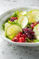 A vibrant close-up shot of a fresh green salad with sliced cucumbers, pickled red onions, and a ruby-red fruit relish, served in a white bowl against a textured background