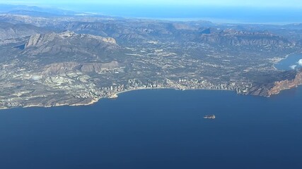 an elevated aerial side view of Benidorm city, in the Valencian coast, taken from a plane cockpit in a sunny summer morning. handheld camera shot - Powered by Adobe