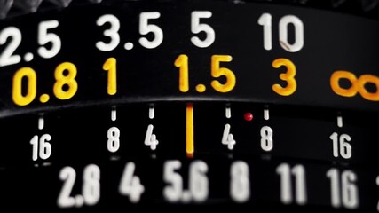 Macro focus pull on black vintage camera lens with orange distance scale numbers - Powered by Adobe