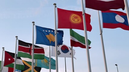 Many colorful national flags wave on a breezy day, with South Korea, Kenya, Kazakhstan, Kyrgyzstan, and Jamaica prominently visible, symbolizing global unity and cultural diversity.