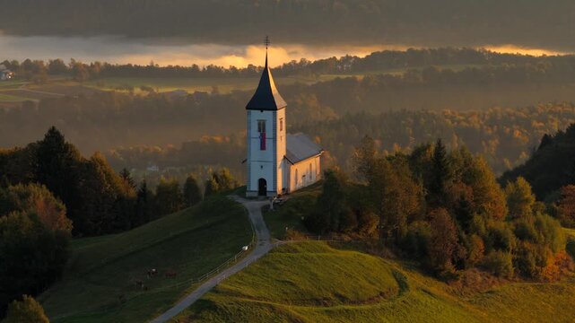 Aerial rising shot of Jamnik church with valley in background, Church of St. Primus and Felician. Foggy morning in Slovenia. Calm and peaceful scene.