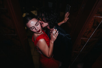 A stylish couple shares an intimate moment in a dimly lit doorway during a night out. The woman...