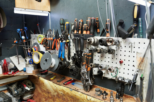 Closeup showing organized assortment of hand tools and bicycle repair equipment hanging on wall in workshop, various screwdrivers, pliers, wrenches and bike parts arranged for maintenance tasks