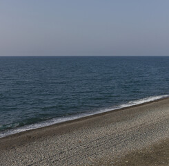 Obraz premium Calm blue sea and pebble beach with clear sky background
