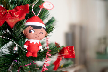 Santa Claus elf doll hangs from a branch of a Christmas tree as part of the festive decoration