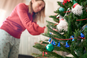 Woman enjoys the Christmas spirit and smiles while hanging bright and colorful ornaments on the tree