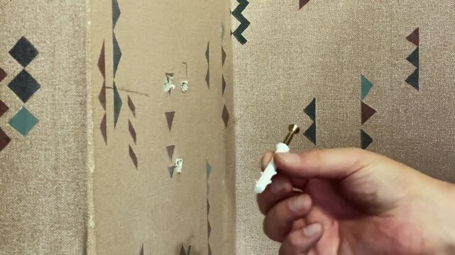 Screw with dowel in hand near the wall with holes