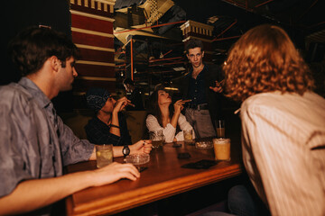 A casual night out with young adults at a bar. They chat, sip cocktails and beer, while one person stands and gestures, creating a lively social scene perfect for lifestyle and nightlife themes.