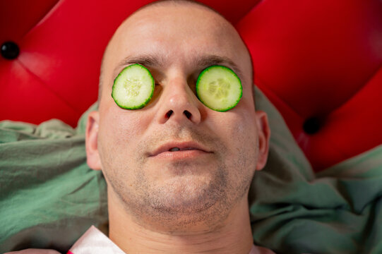 Short-haired man with cucumber slices on his face enjoying a skincare and relaxation routine.