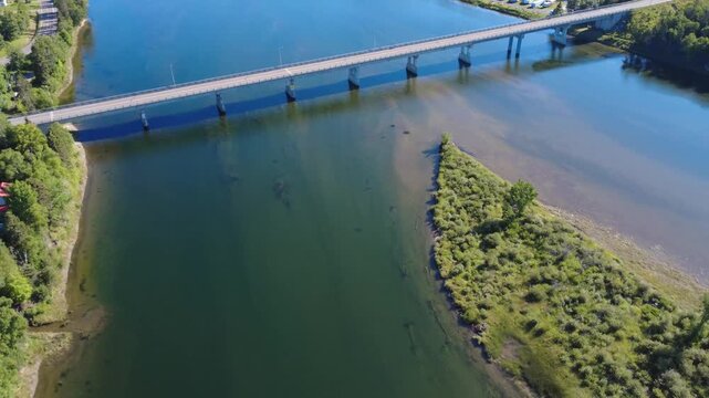 Aerial view of the beam bridge spanning the Cascapedia salmon river, where it is divided in two by a verdant island. Quebec, Canada, 2025.