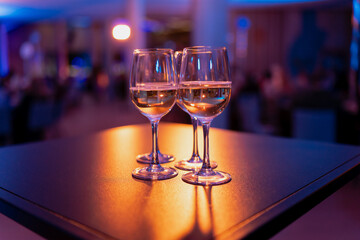 Closeup of three wine glasses arranged on table in indoor banquet space with decorative illumination, symbolizing catering service, beverage presentation and restaurant atmosphere