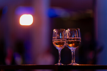 Pair of wine glasses filled with golden liquid under ambient event lighting, artistic concept of togetherness, celebration, fine dining and refined hospitality design