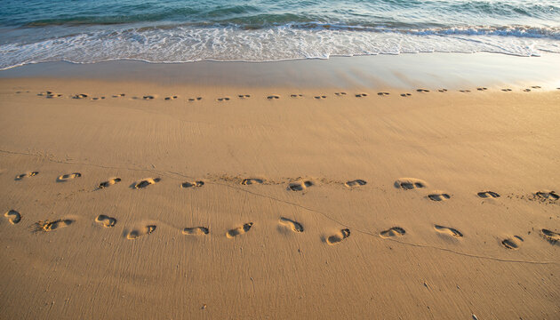 Footprints in smooth sand lead toward ocean under golden sunlight, creating peaceful and cinematic beach scene with gentle waves and clear sky in background