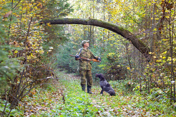 A hunter and his hunting dog stand on a forest road under a tree arch