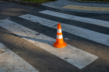 An orange traffic cone stands on a worn crosswalk, casting long shadows in the soft light of late afternoon