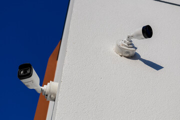 Two security cameras are installed on a white wall, providing surveillance and protection in a clear sky setting