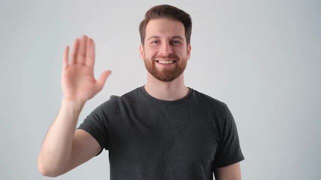 A smiling man with a beard waves hello with his right hand.