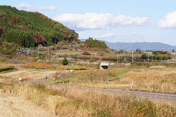 秋の青空の下、線路や畑、山々が広がる日本の里山の風景