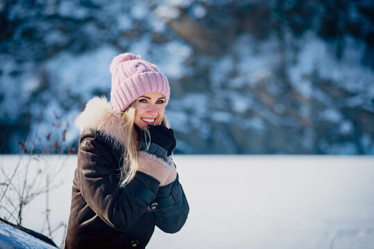 Portrait of beautiful smiling young woman on winter day. Young woman strolling in winter, surrounded by snow and ice. Peaceful lake view under a sunny sky