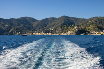 From a cruise ship, we see the ship's wake and, in the background, Monterosso al Mare and the mountains. Cinque Terre, Italy